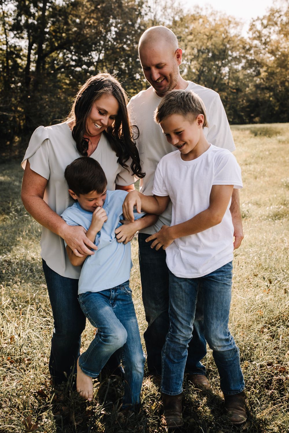 Family shares playful moment together in a sunlit field during golden hour photo session.