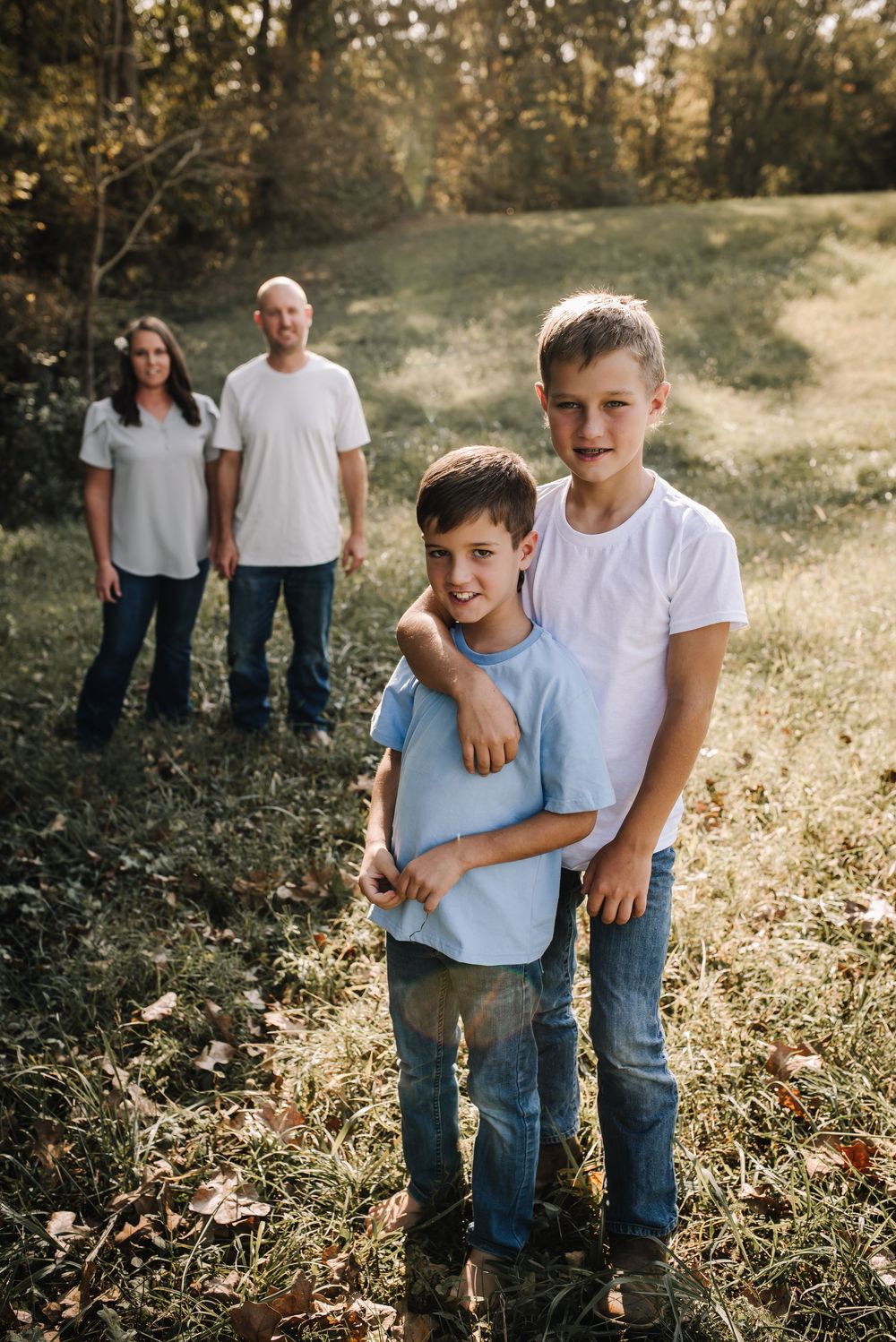 A family poses together in a sunlit outdoor setting wearing casual blue jeans and light colored shirts.