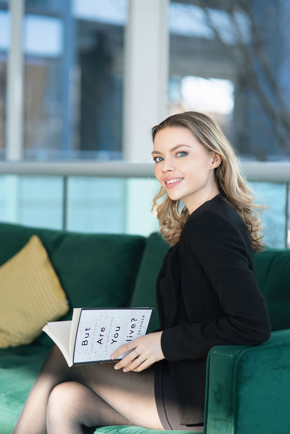 Woman in black sweater relaxes on emerald green couch while reading a book.