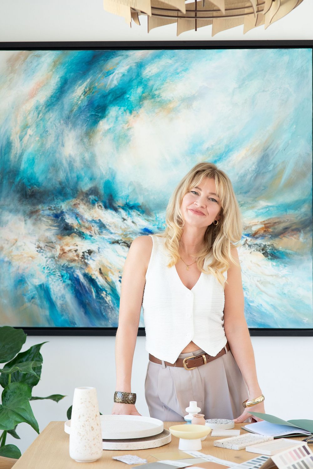 Interior designer working at desk with samples and materials against large blue abstract seascape painting.