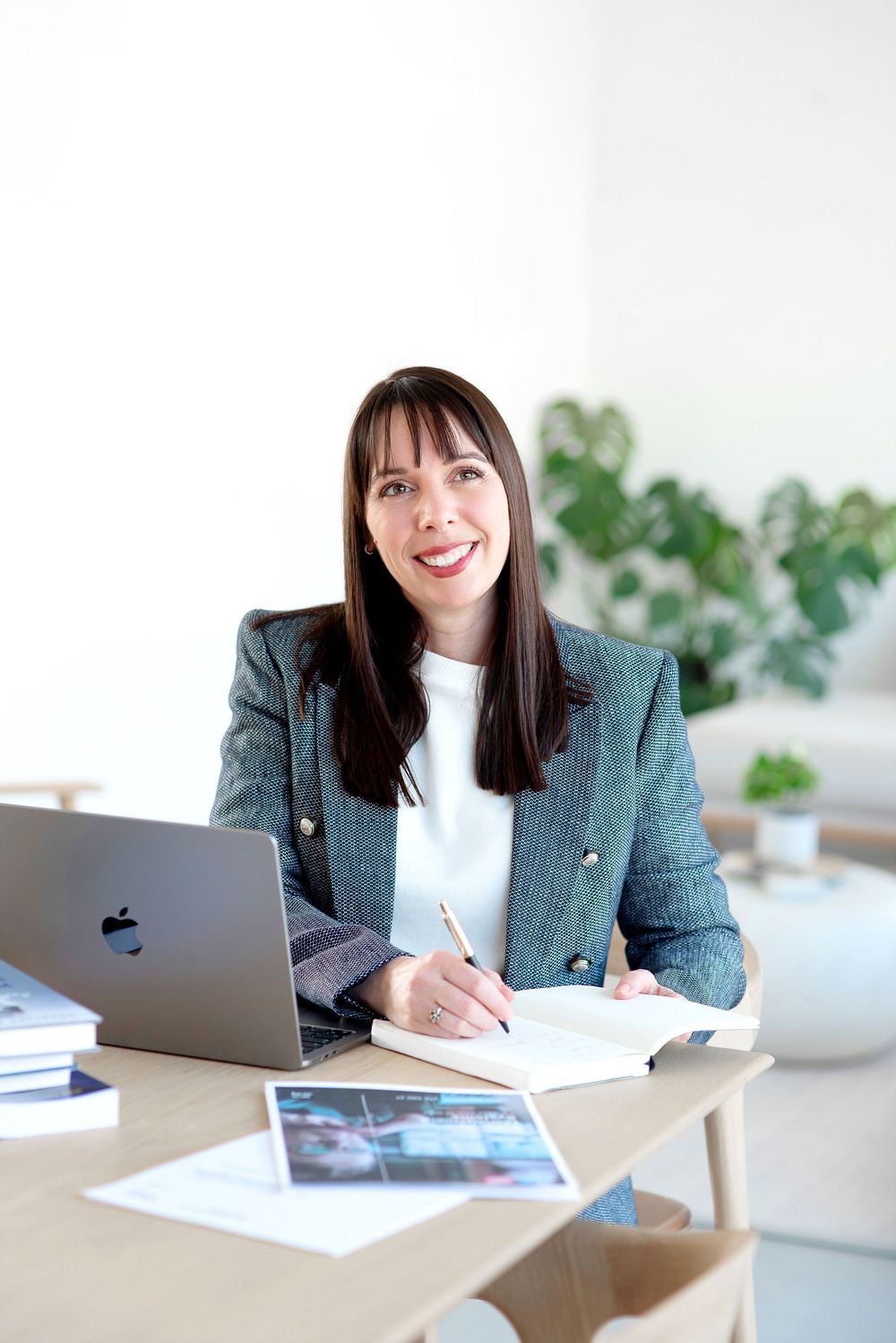Professional working at desk with laptop and documents in bright modern office with plants in background.