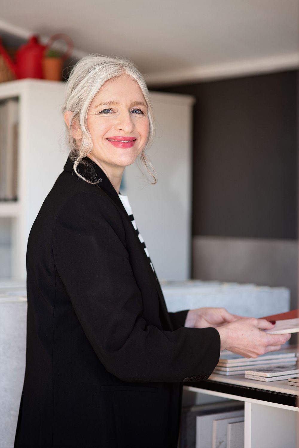 Professional woman in black blazer smiling while organizing documents at a desk in an office setting.