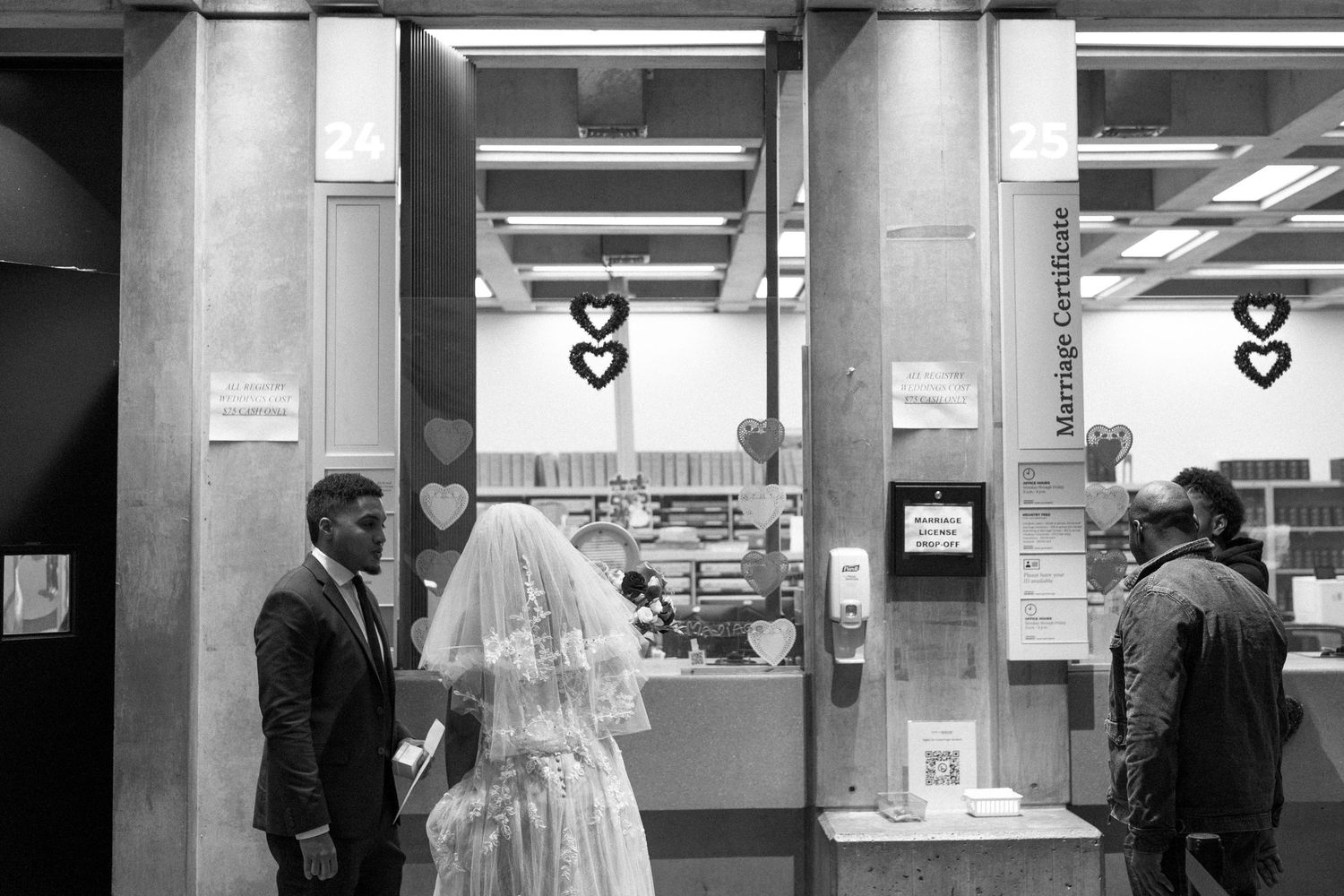 A black and white photograph shows a person standing at a service counter in what appears to be a bank or office.