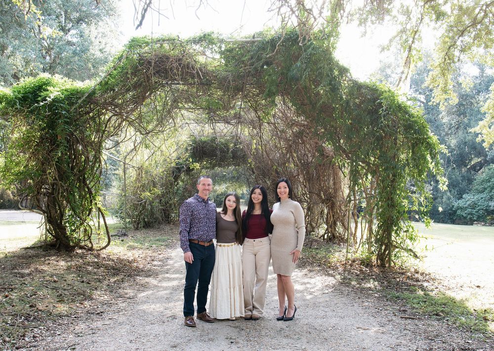 Family of four stands under ivy-covered arch on garden pathway.