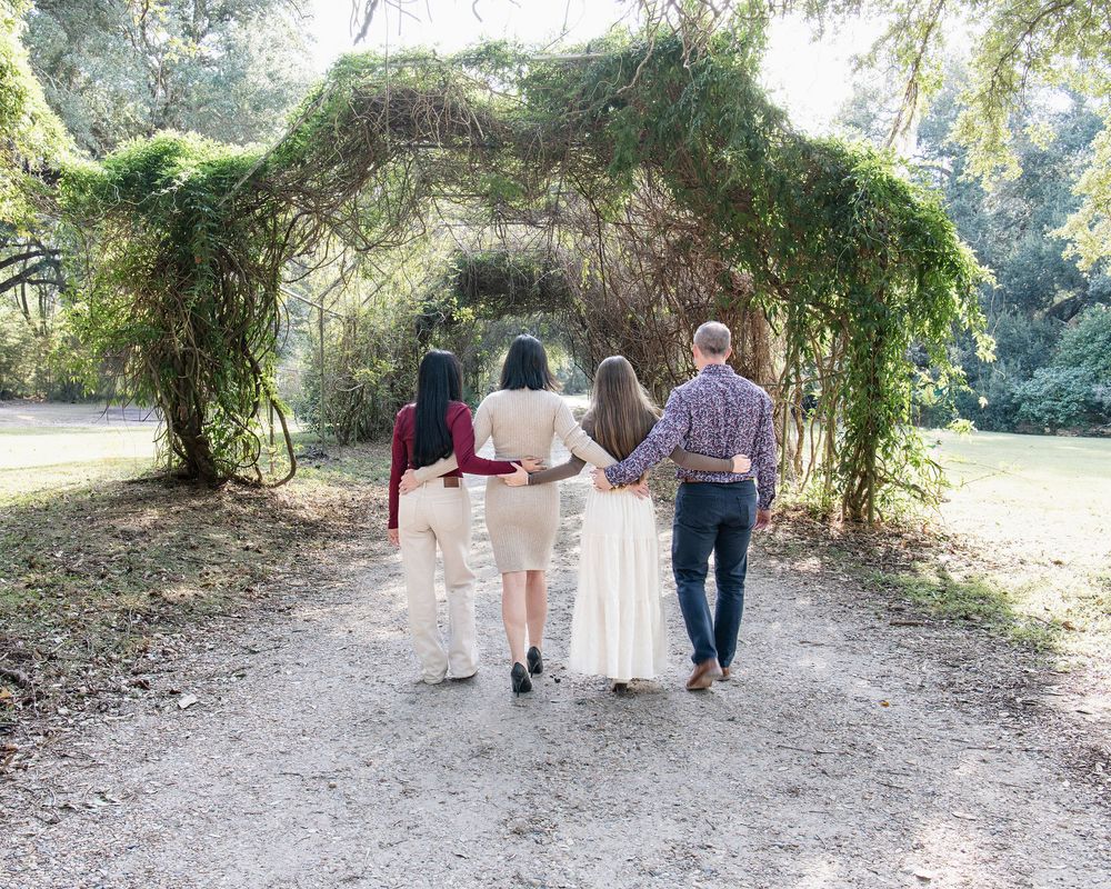 Family of four walks hand-in-hand under vine-covered arch in park.