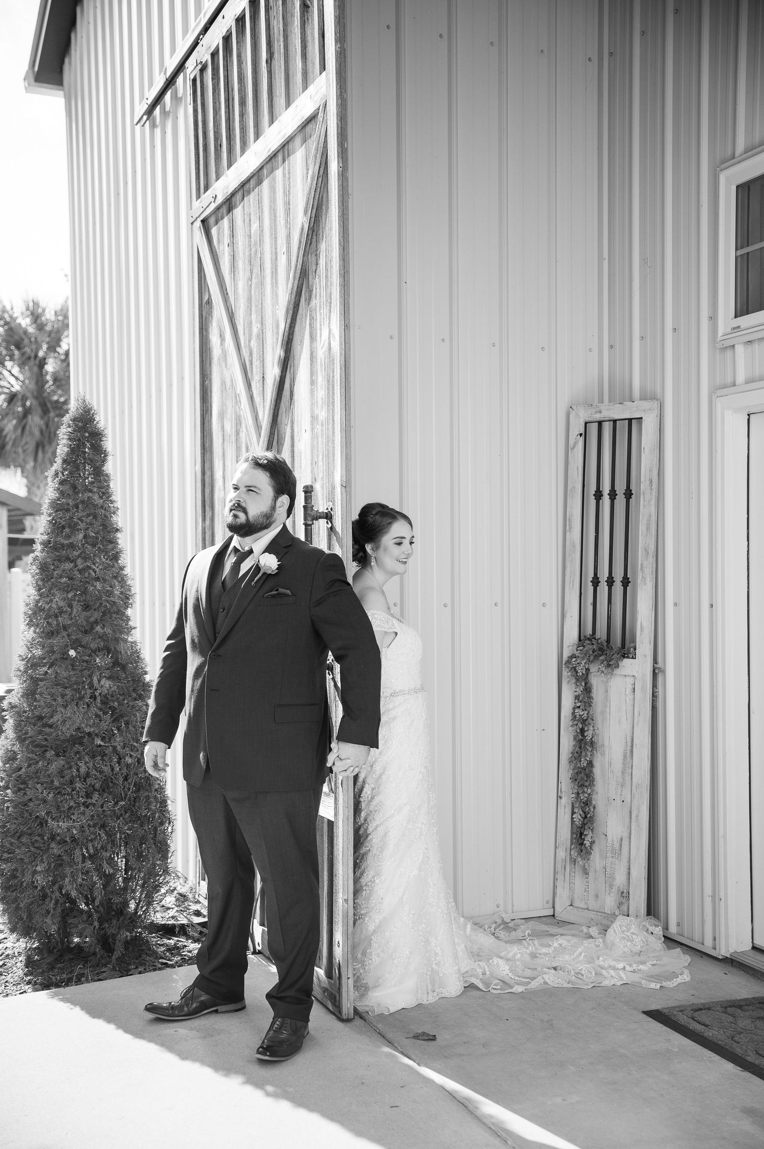 Wedding couple stands against white barn exterior in artistic composition.