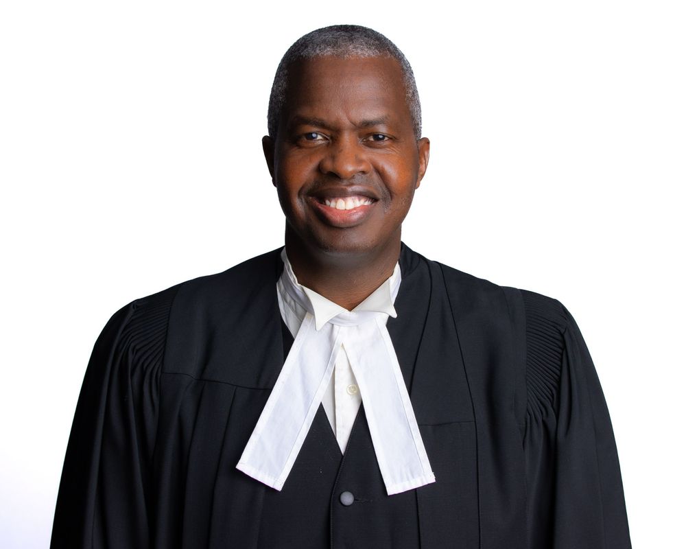 Three legal professionals wearing traditional black robes and white court bands stand together smiling.