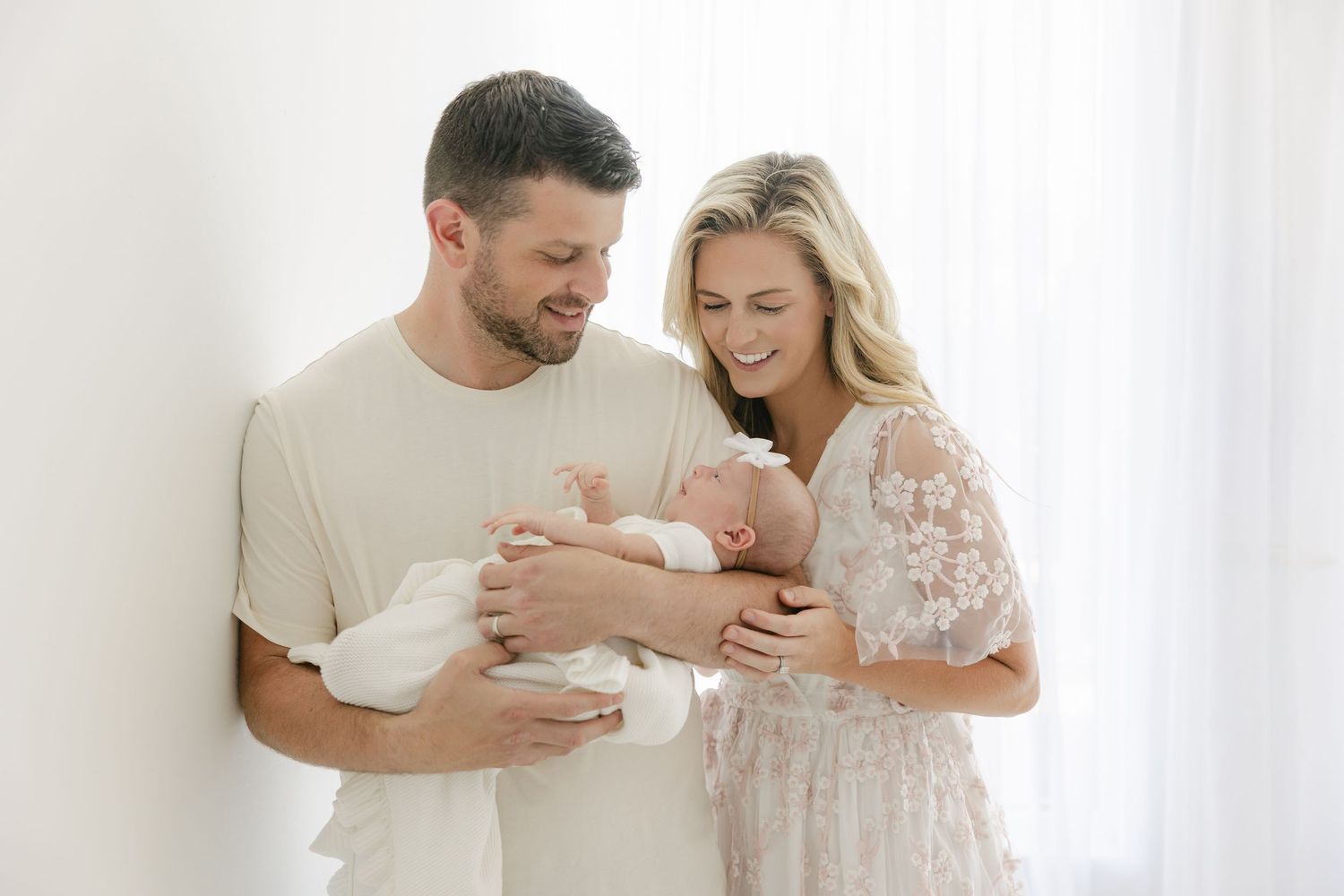 Parents lovingly hold and gaze at their newborn baby in a bright white room.
