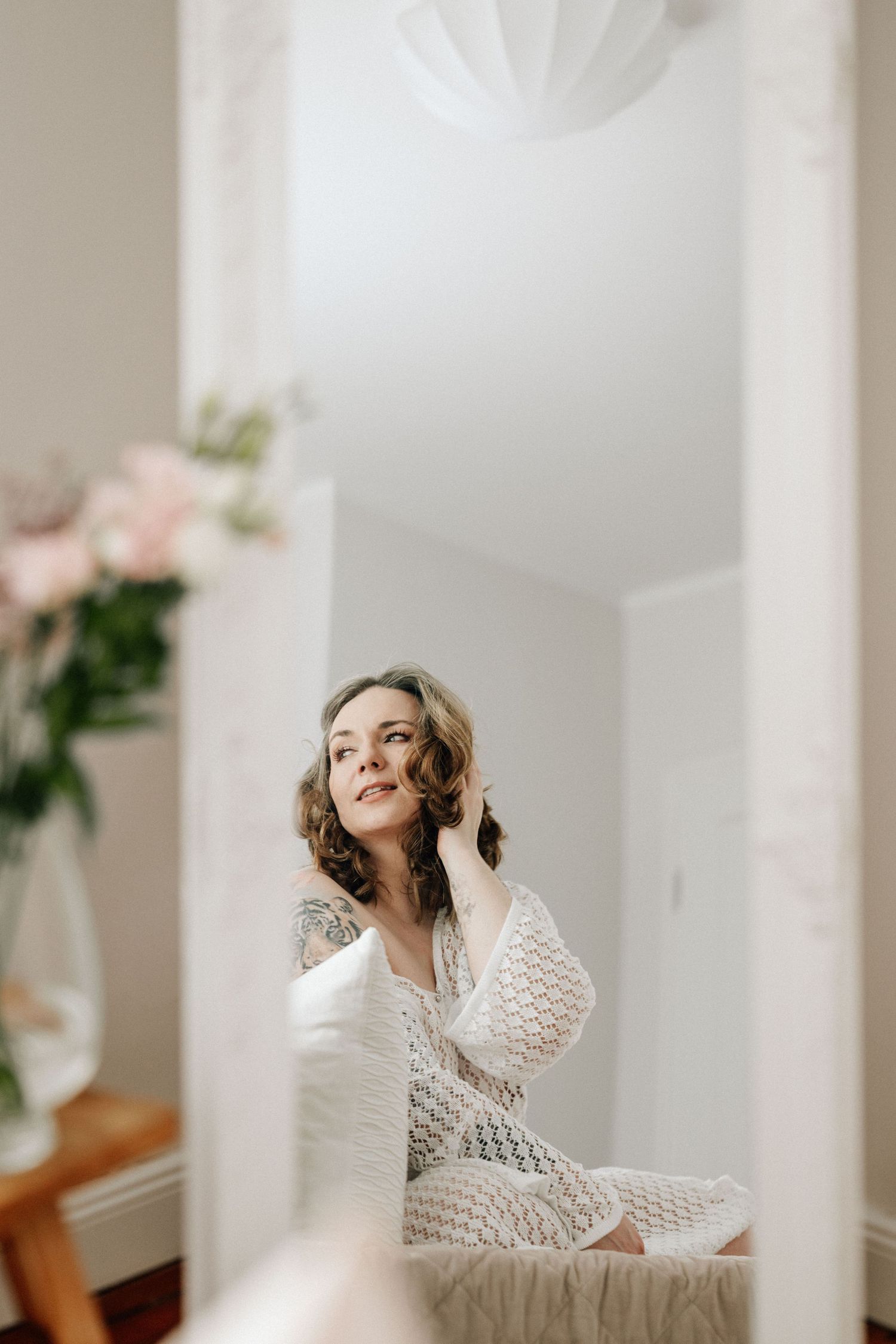 kreatives Portrait einer Frau im Strickkleid über einen Spiegel im natürlichen Fotostudio von Julia Aßmann