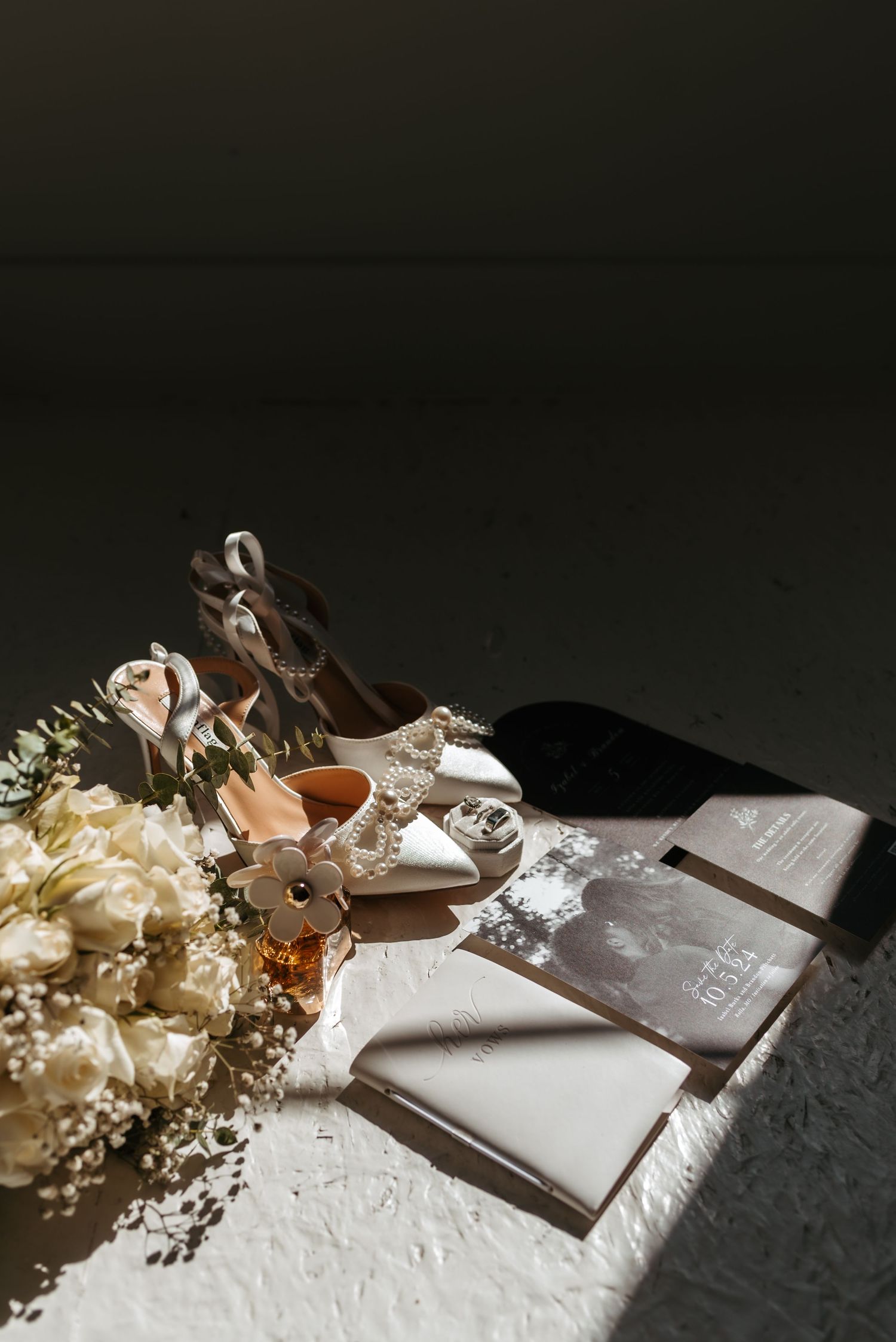 Wedding details including elegant shoes, dried baby's breath flowers, and an open book on a white textured surface.