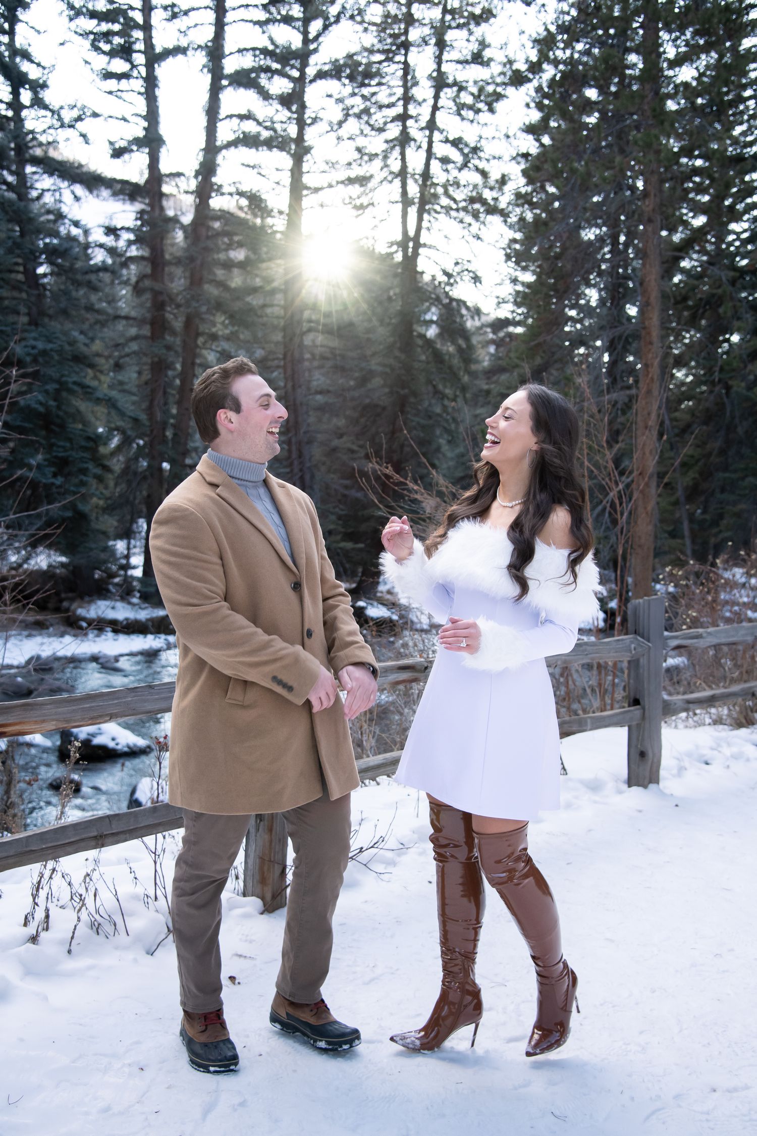 Cute candid photo of a chic and fashionable couple laughing together with sun shining though during winter Vail engagement photos.