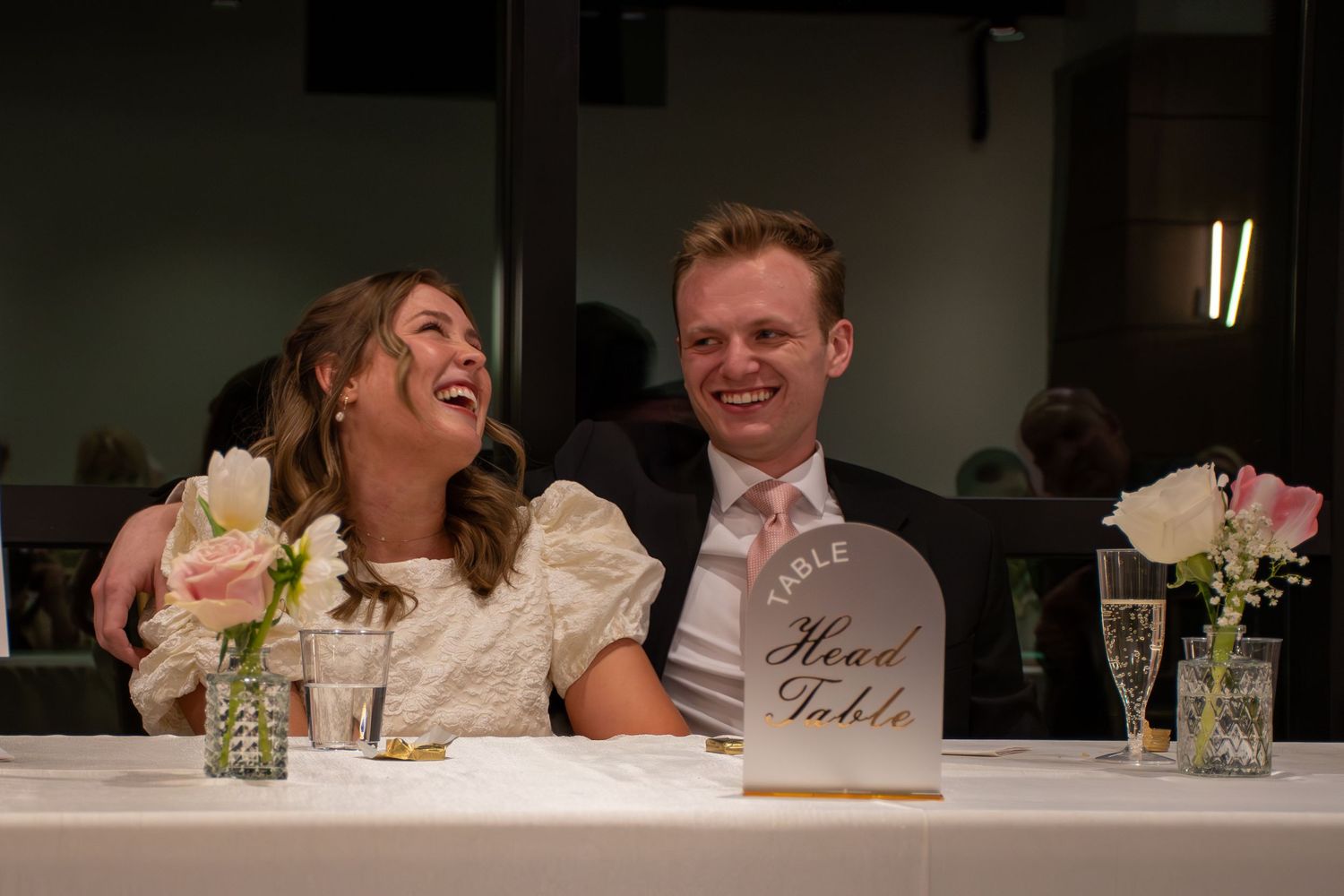 A couple shares a romantic kiss during their wedding reception in an intimate indoor venue setting.