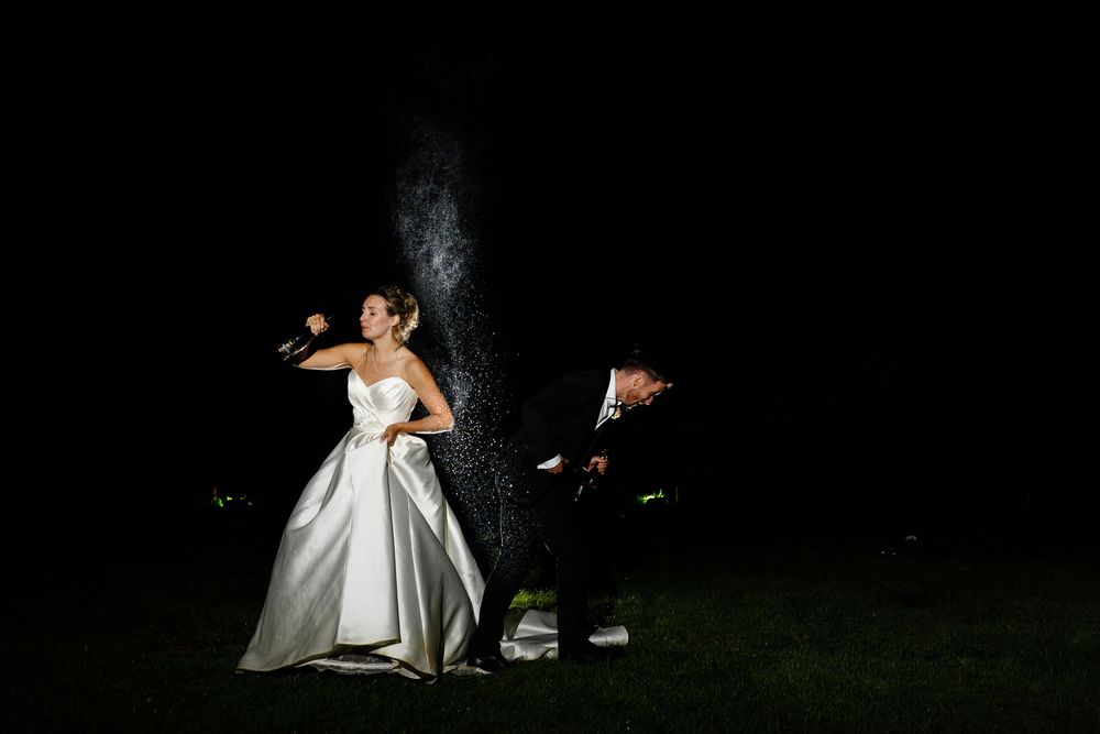 A bride in a white satin gown stands in a dark garden while sparklers create magical light trails behind her.