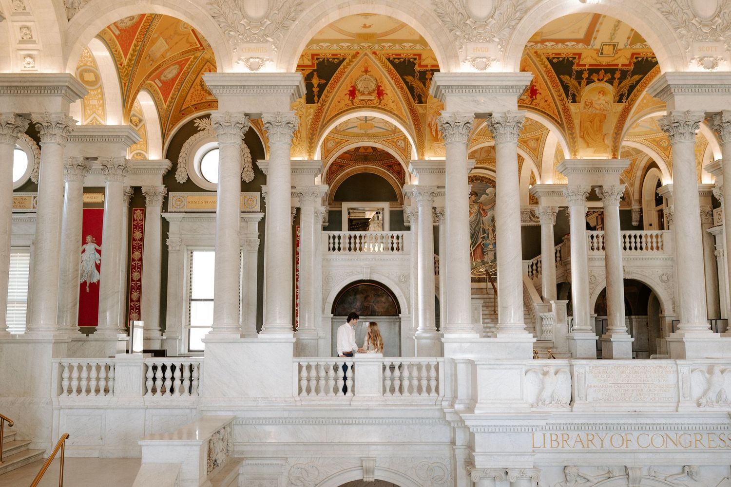 Couple poses on grand marble staircase inside ornate Library of Congress Great Hall.