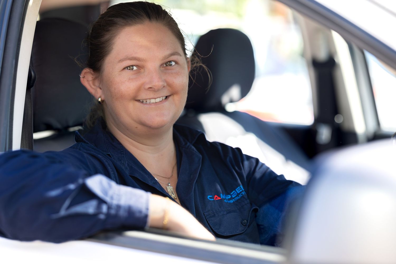 Four people sit in a car and smile at the camera while wearing matching blue uniforms.