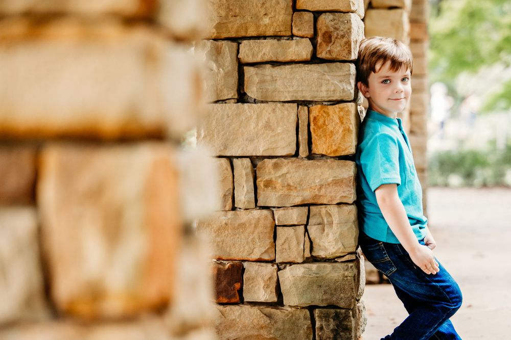 A child in a turquoise shirt sits on a stone wall surrounded by rustic architectural elements in warm lighting.