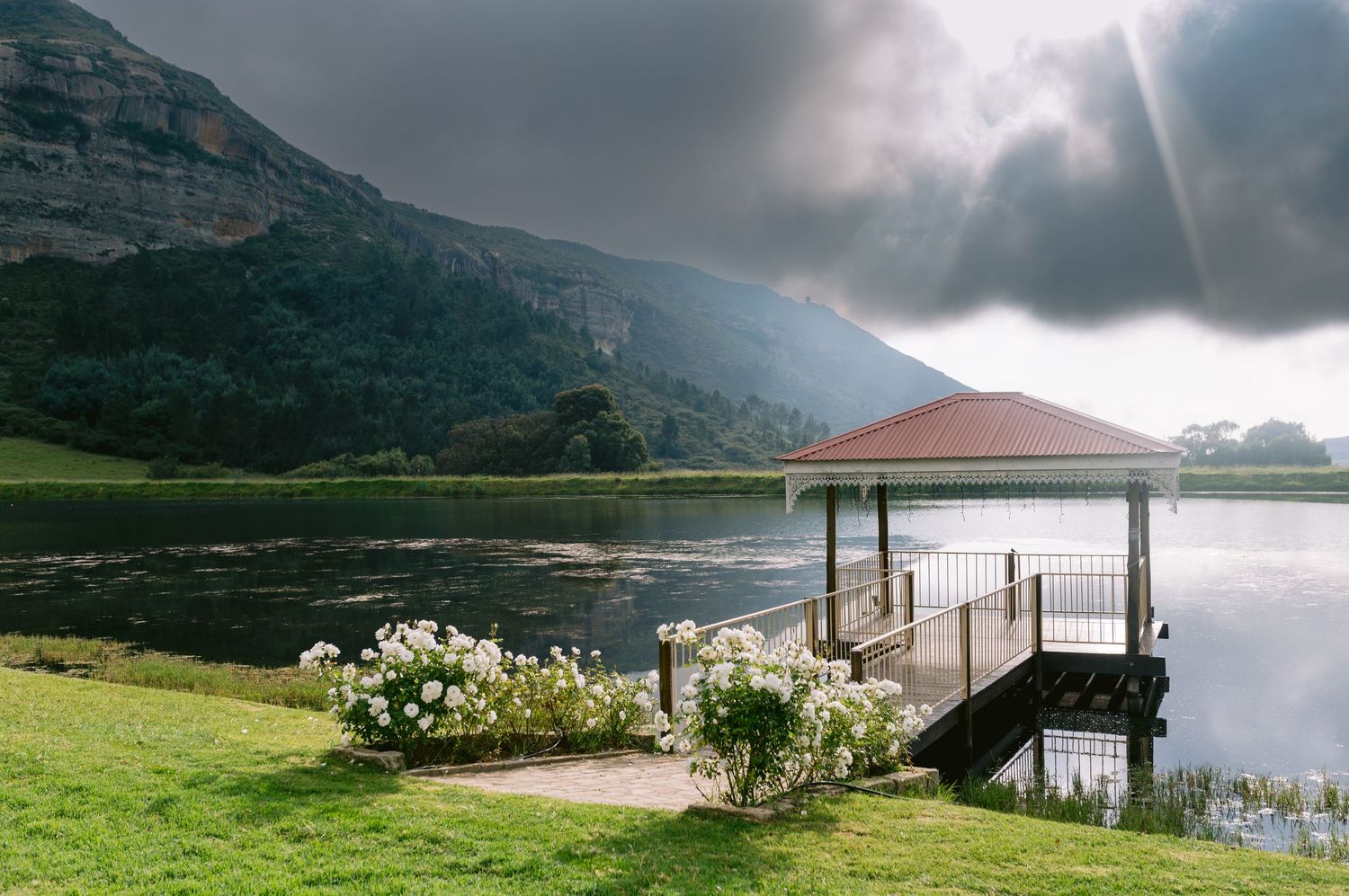 Panoramic view of a dramatic stormy coastline with mountains, houses, and a wooden pier extending into the water.