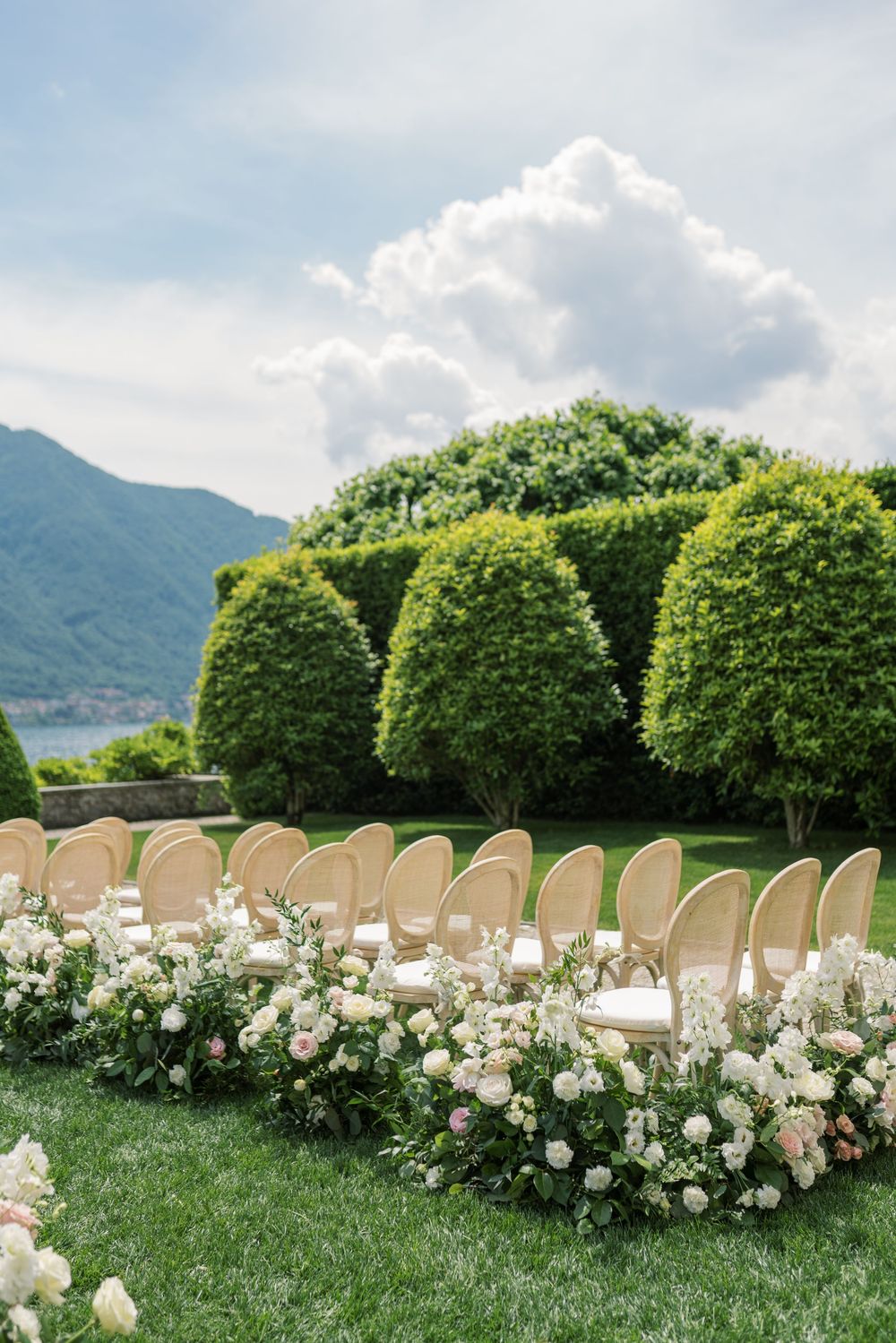 Outdoor wedding ceremony setup with elegant chairs and floral decorations overlooking a mountain lake.