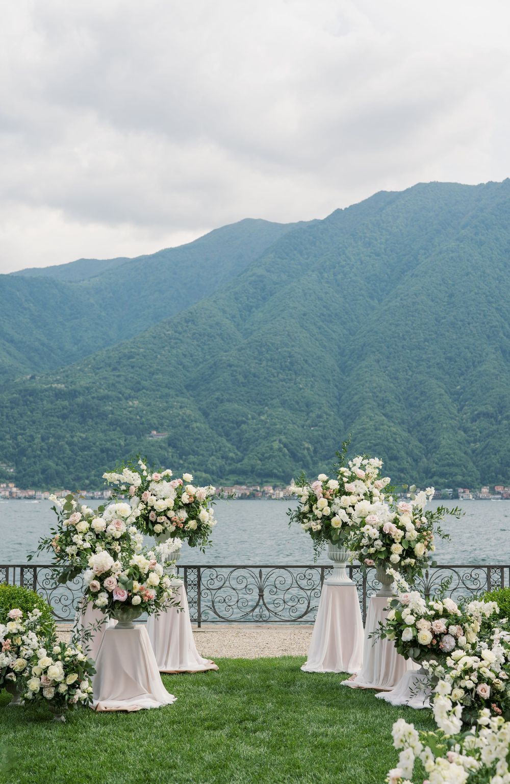 Wedding ceremony setup with white floral arrangements and mountain lake backdrop in an elegant garden.