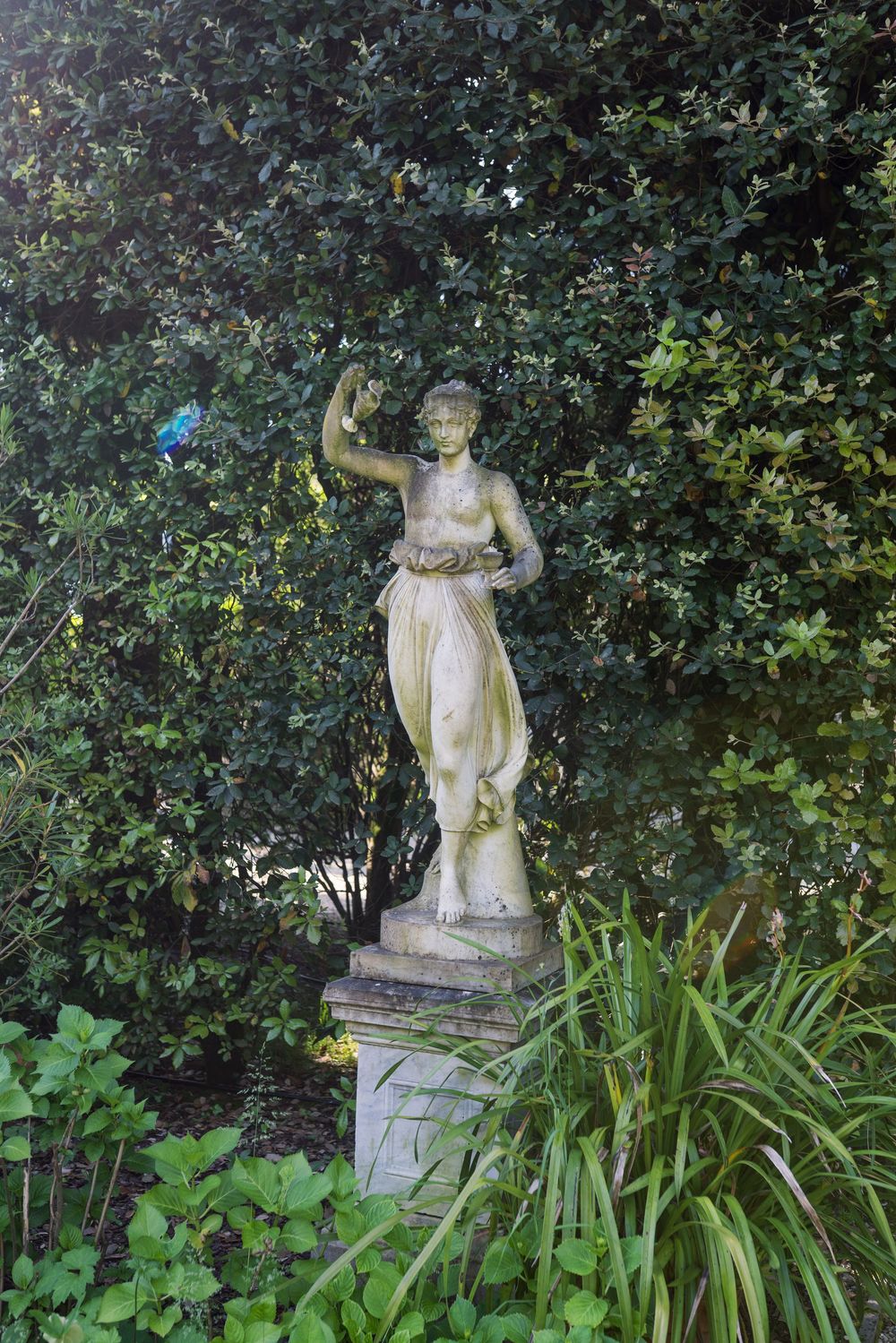 Classical stone statues nestled among lush garden foliage and hedges.