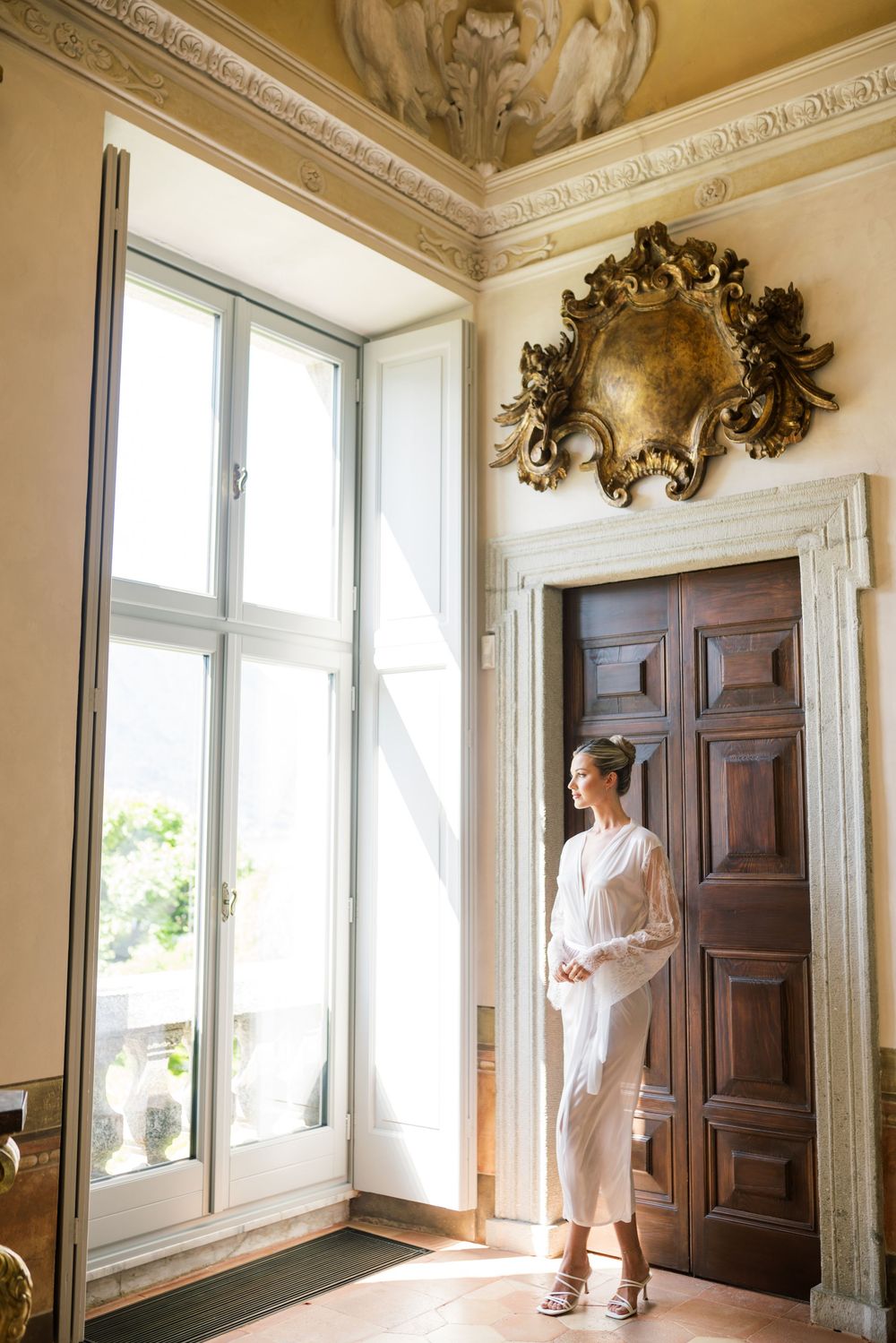 Sunlit classical room with ornate moldings, tall windows, and wooden doors.