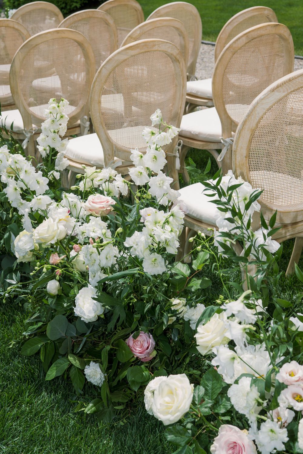 Elegant wedding ceremony seating with cane back chairs and white floral aisle decorations.