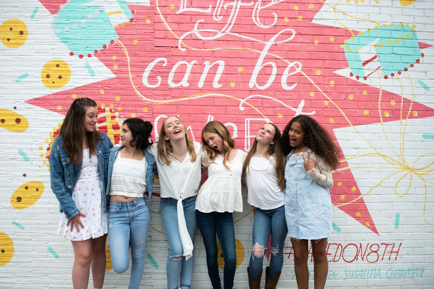 Group of friends laughing and having fun against colorful graffiti wall with emoji designs.