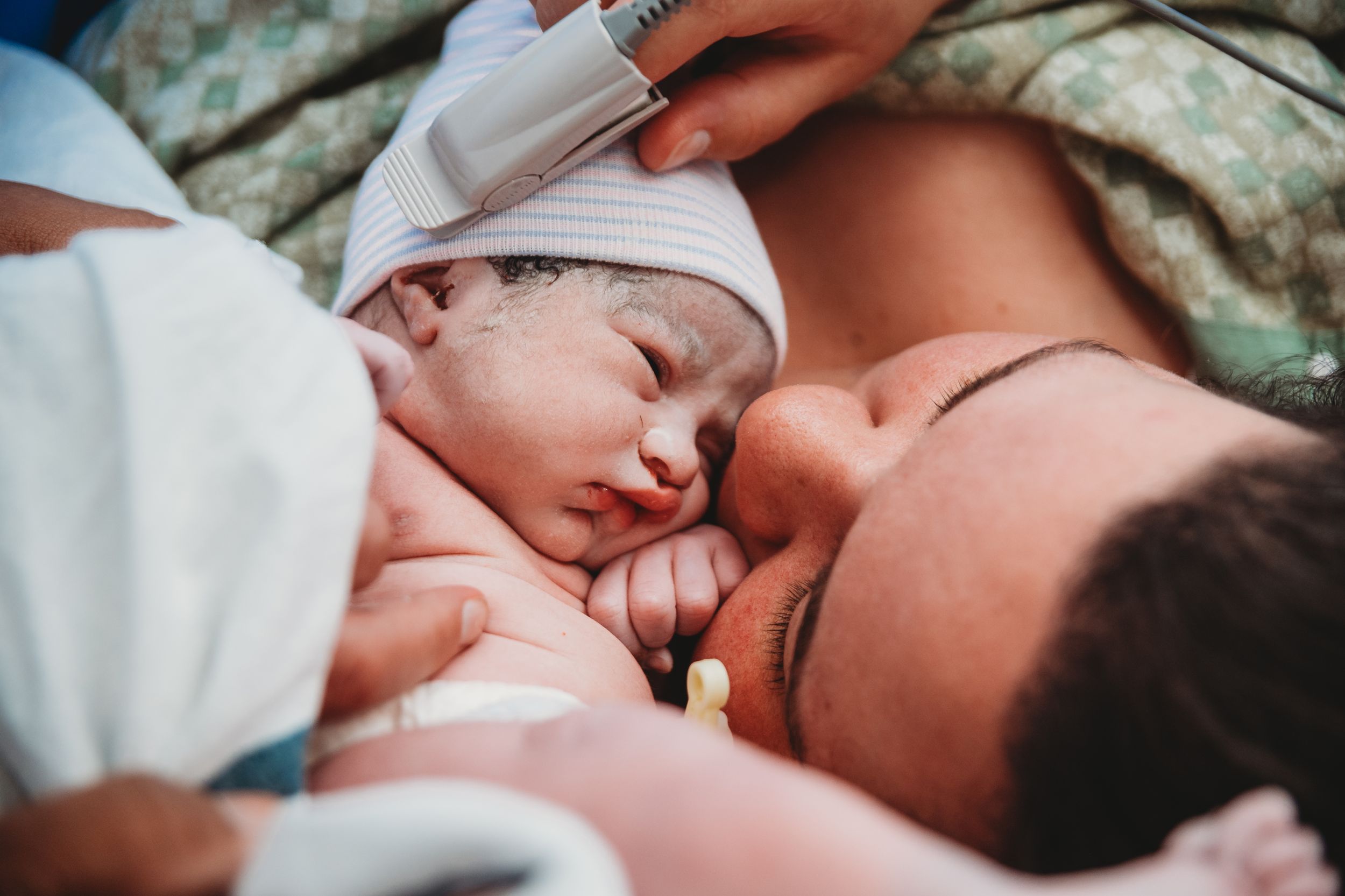 A tender moment between parent and newborn baby lying together in white blankets.