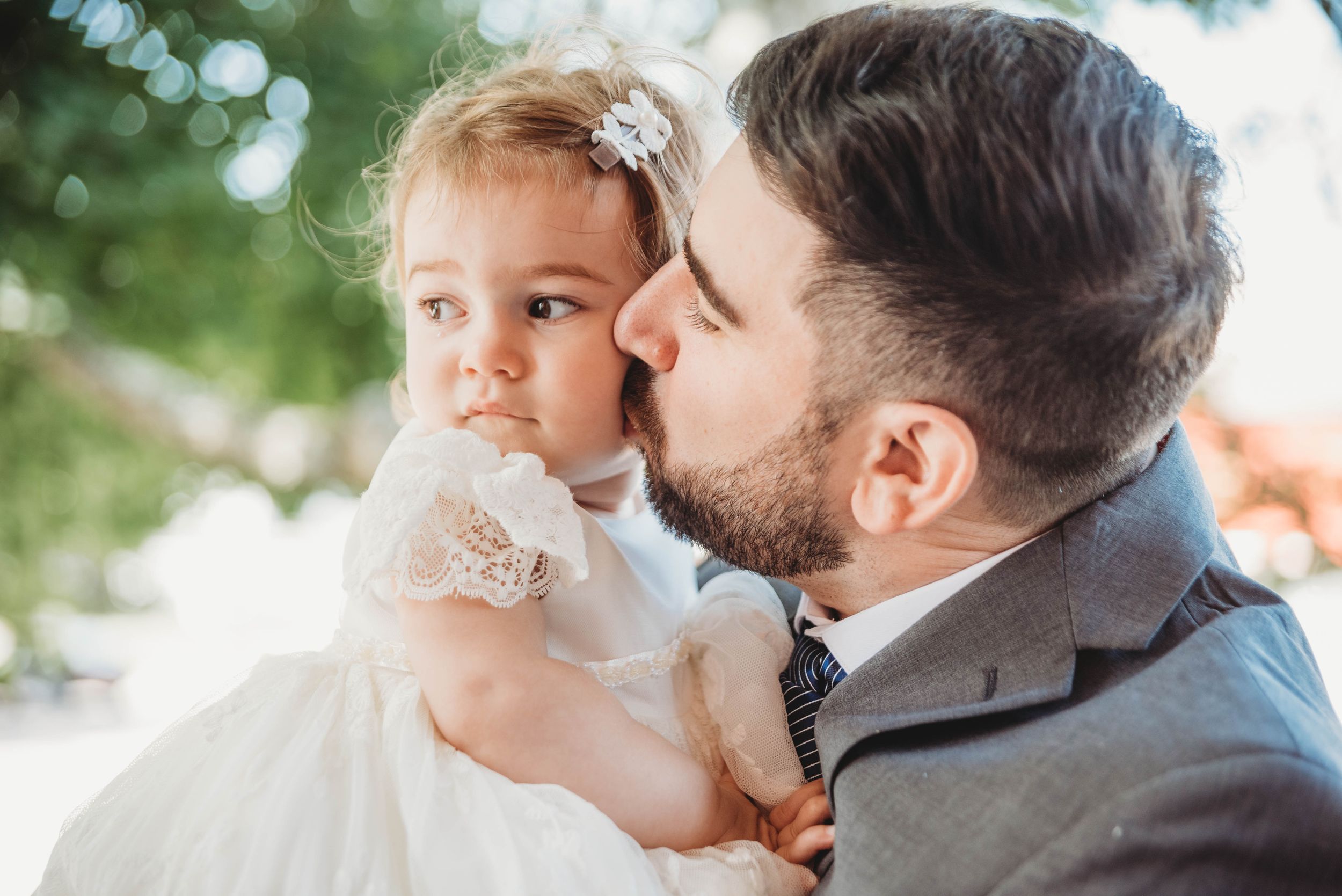 A romantic couple shares tender moments during their outdoor wedding photoshoot in a sun-dappled garden setting.