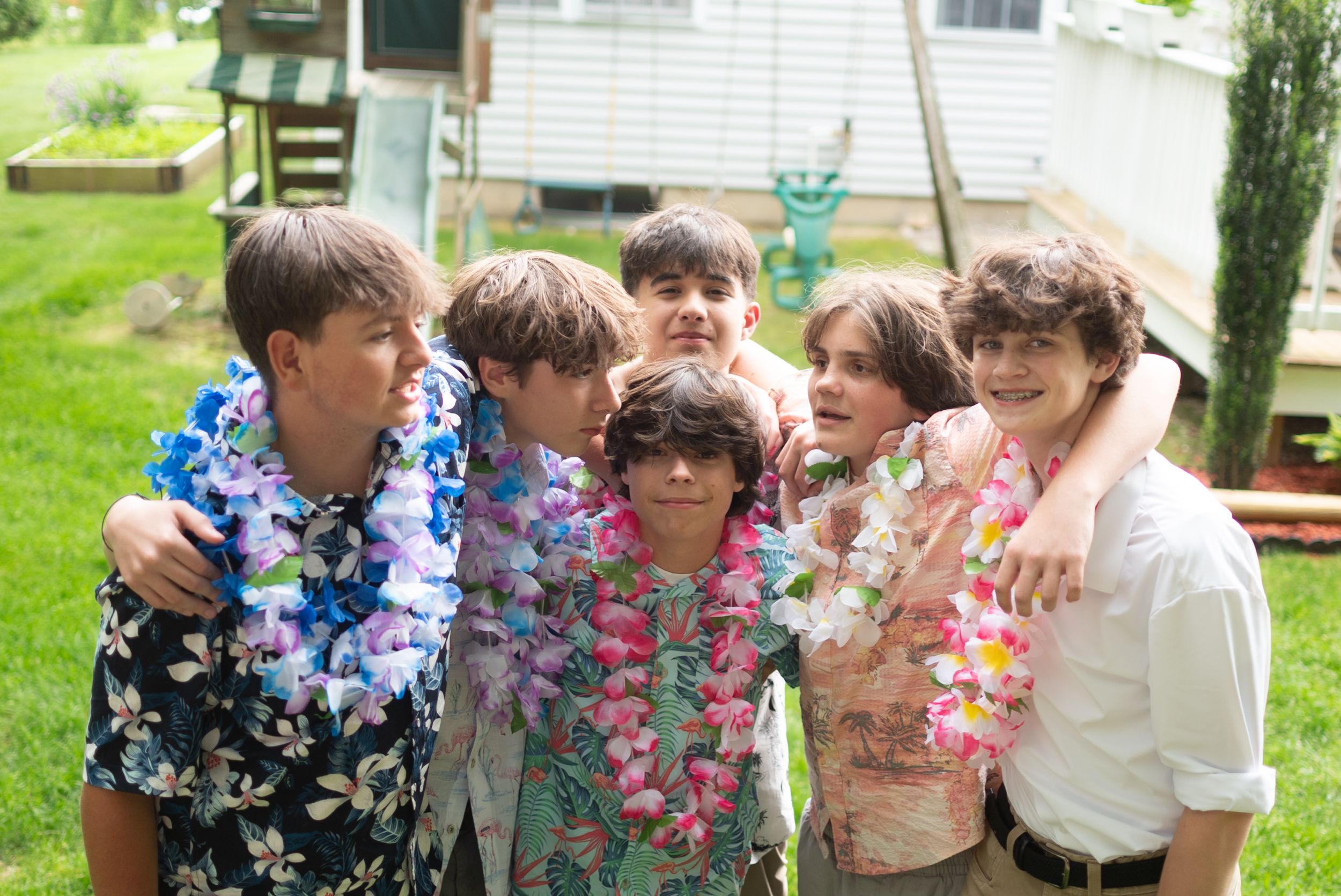 A group of people wearing colorful leis and party attire celebrate outdoors in a festive summer gathering.