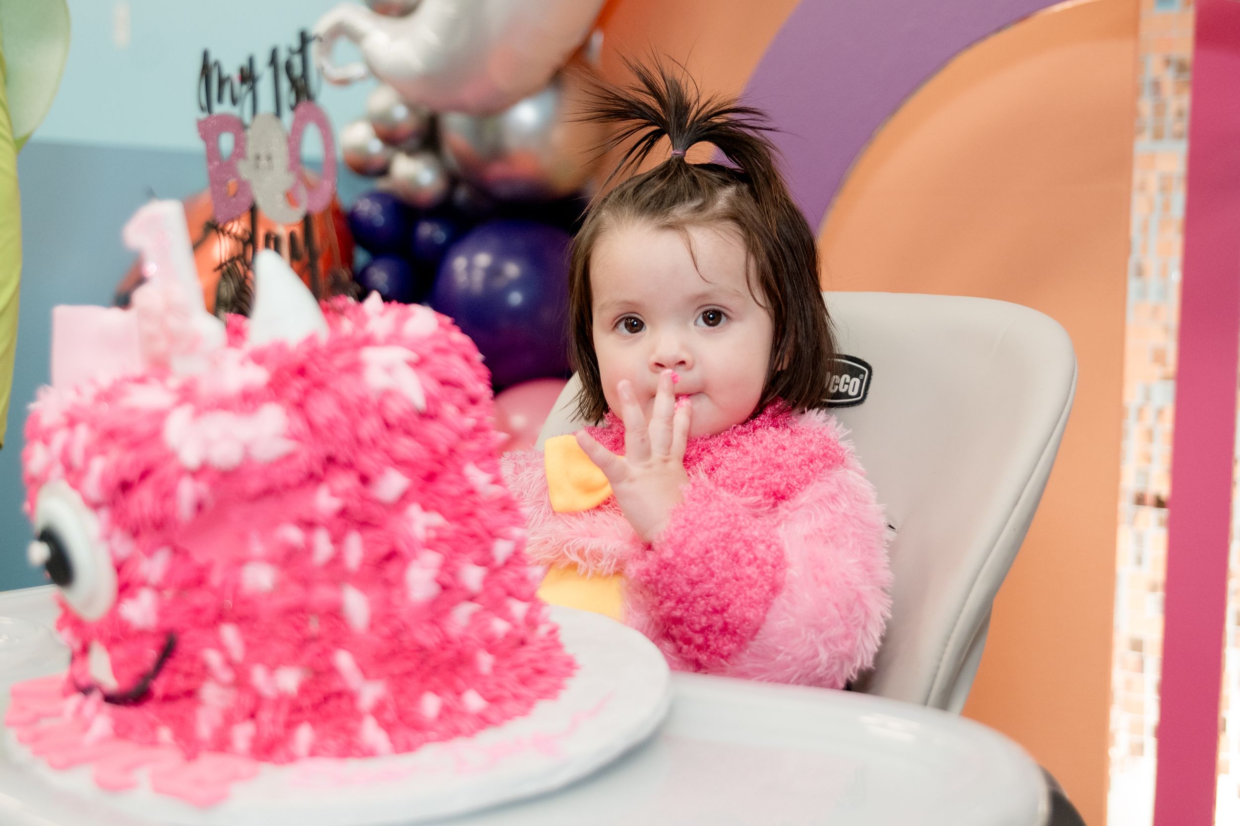 Pink and white birthday cake decorations with sprinkles and frosting displayed on a colorful table setting.