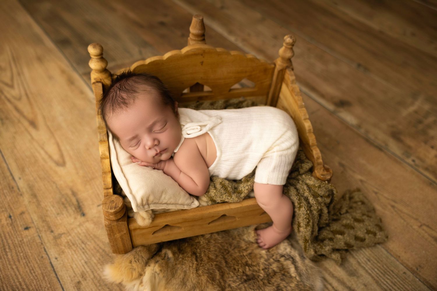 A newborn baby girl laying her chin on her hands in a yellow bucket on a wooden floor.