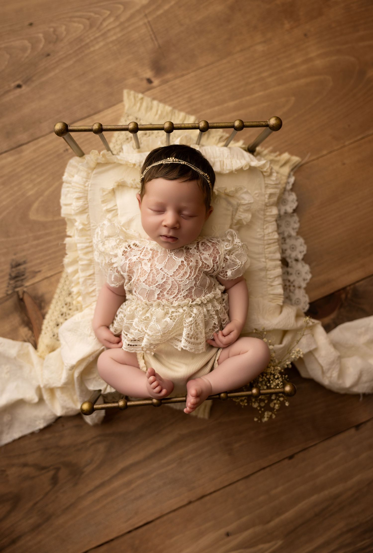 A newborn baby girl laying her chin on her hands in a yellow bucket on a wooden floor.
