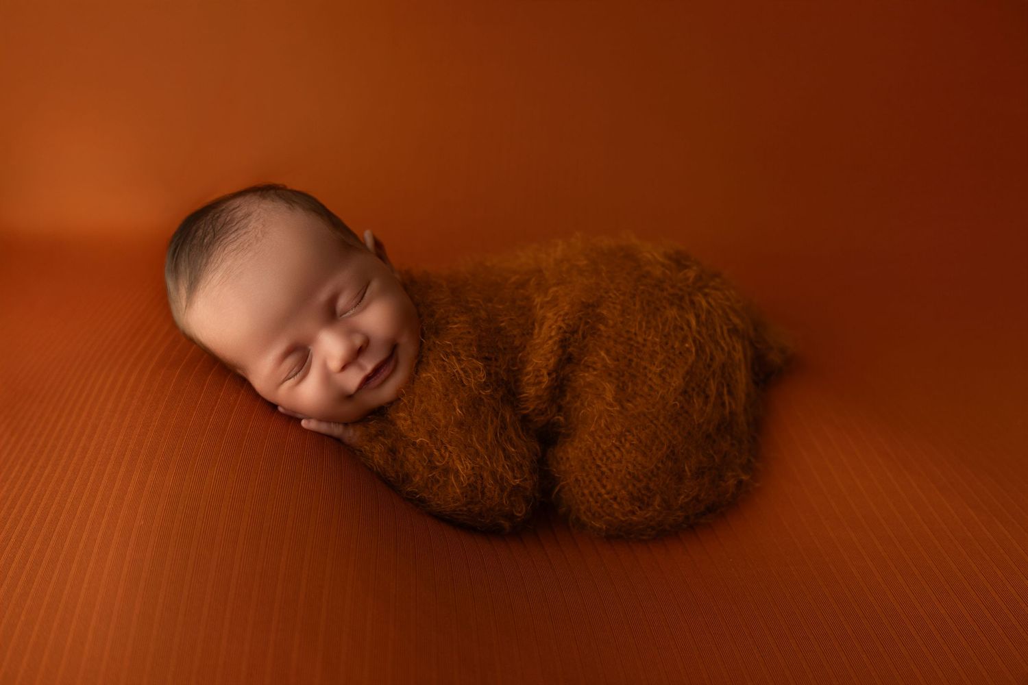 A newborn baby girl laying her chin on her hands in a yellow bucket on a wooden floor.