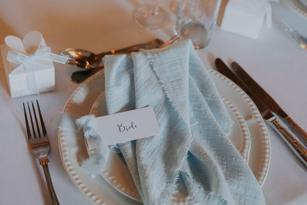 Bride place setting with blue linen napkin, white charger plate, and small gift box.