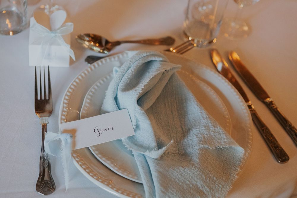 Groom place setting featuring light blue napkin, decorative white plate, and elegant cutlery.