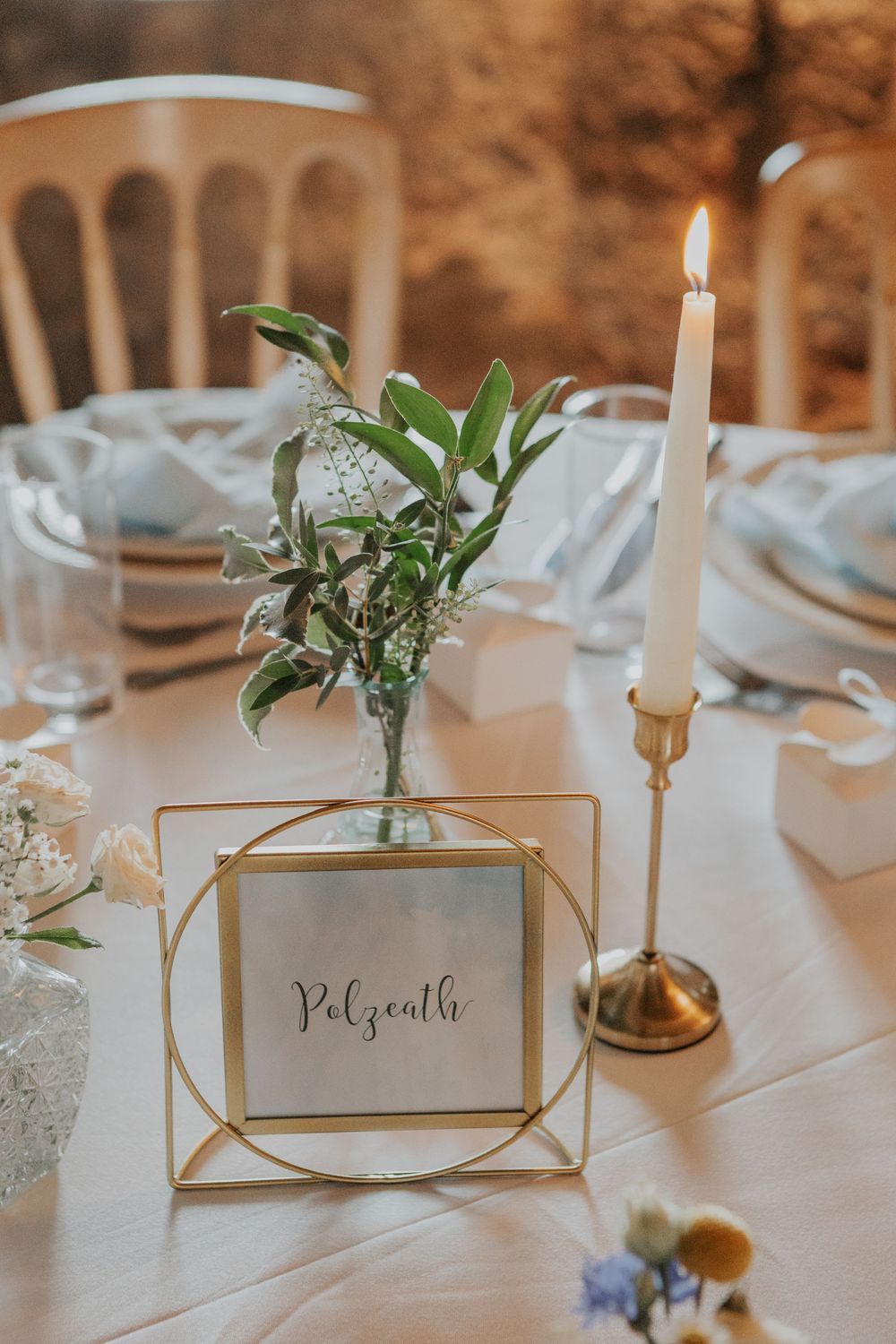 Gold geometric wedding table number frame reading Polzeath with a bud vase and lit taper candle.
