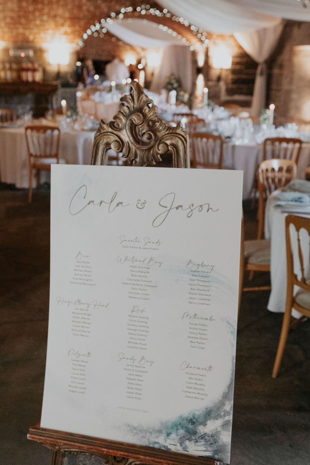 Wedding seating chart for Carla and Jason displayed on an ornate gold easel in a brick venue.