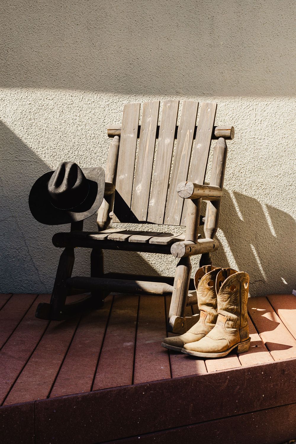 Cowboy boots and a hat cast dramatic shadows on a wooden deck in bright sunlight.