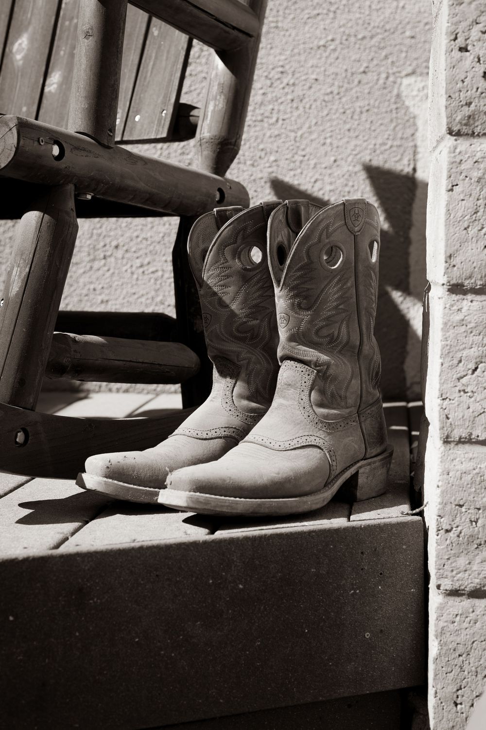 A row of worn cowboy boots lined up on a wooden shelf in black and white.