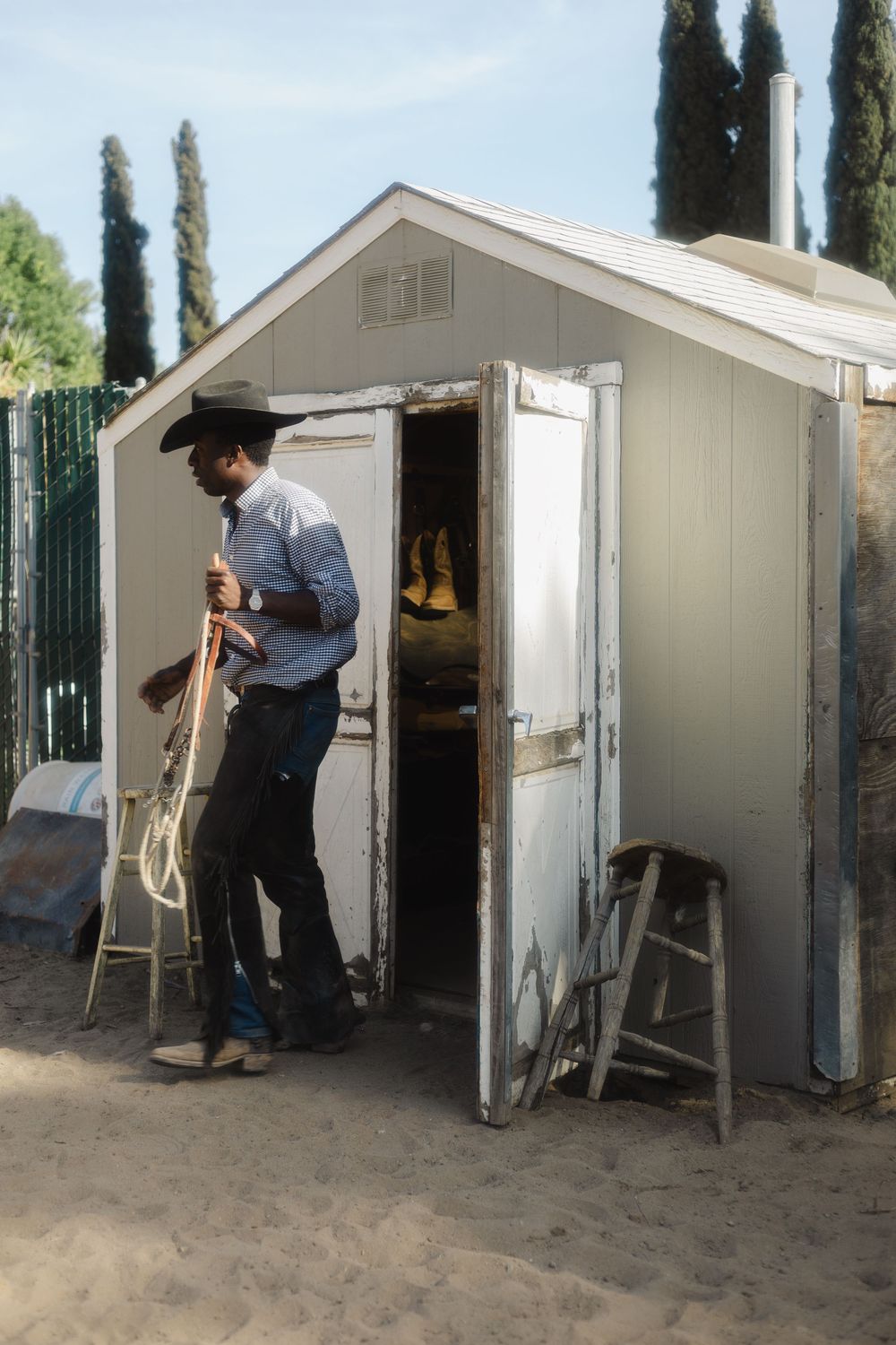 White storage sheds with people moving equipment near cypress trees.