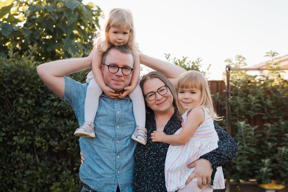 daughter sits on dad shoulder older and mom holds older daughter in her hands in their rouse hill home in Sydney during a family photoshoot