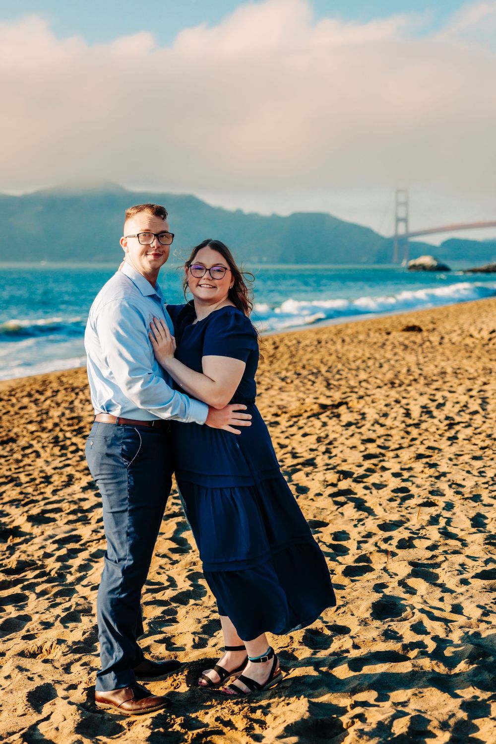 Couple sharing tender moments on Baker Beach with iconic San Francisco bridge in the distance.
