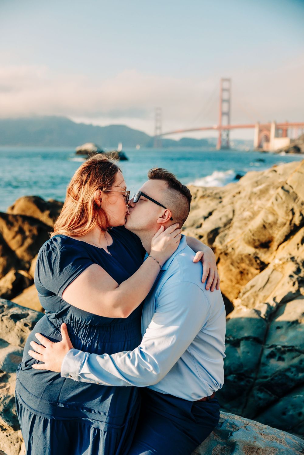 A romantic photoshoot on rocky coastal terrain with the iconic Golden Gate Bridge visible in the background.