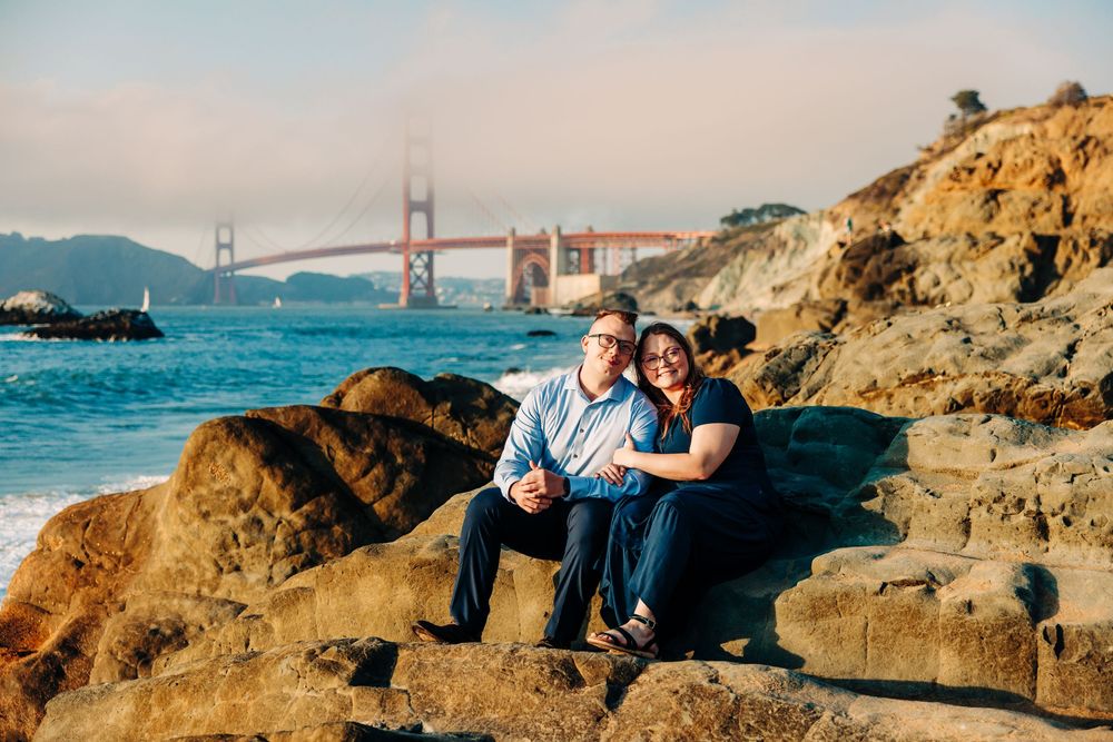 Couple sitting together on coastal rocks with iconic Golden Gate Bridge in San Francisco Bay.