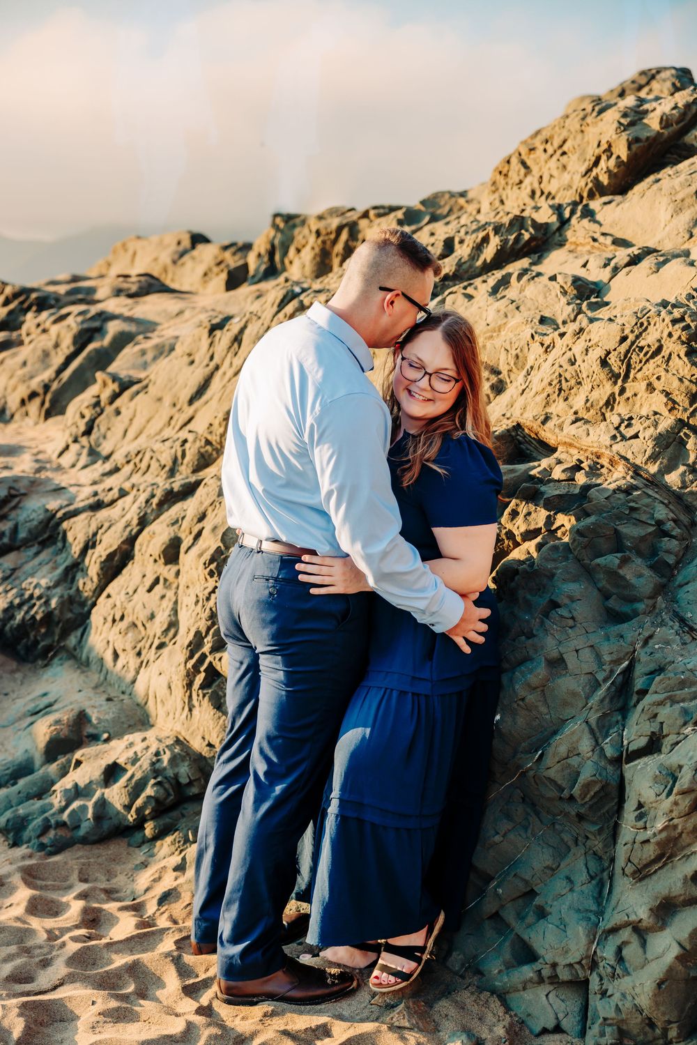 Romantic photoshoot on rocky beach cliffs with San Francisco Bay and bridge in the background.