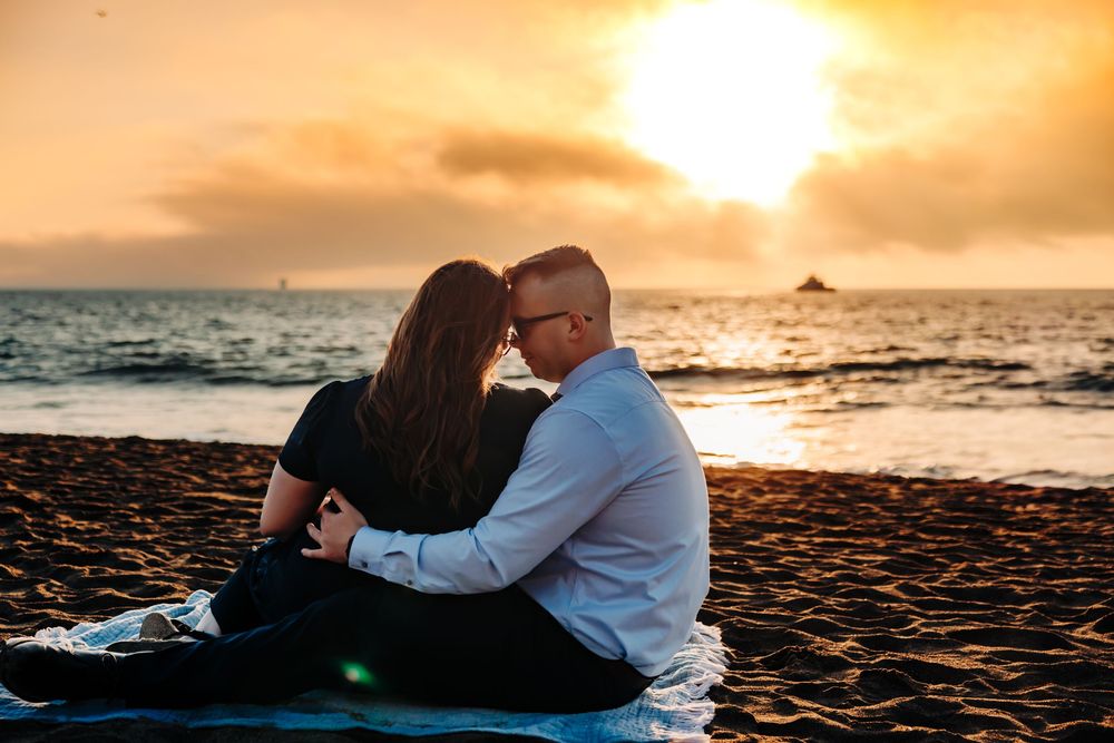 A couple shares an intimate moment on the beach during a golden sunset over the Pacific Ocean.
