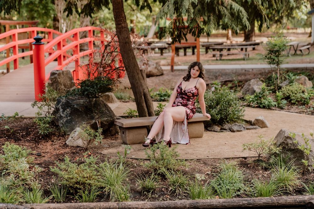Casual portrait on a bench near a red Japanese bridge in a garden setting.