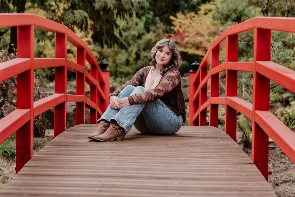 Relaxed pose on a red wooden bridge surrounded by evergreen trees.