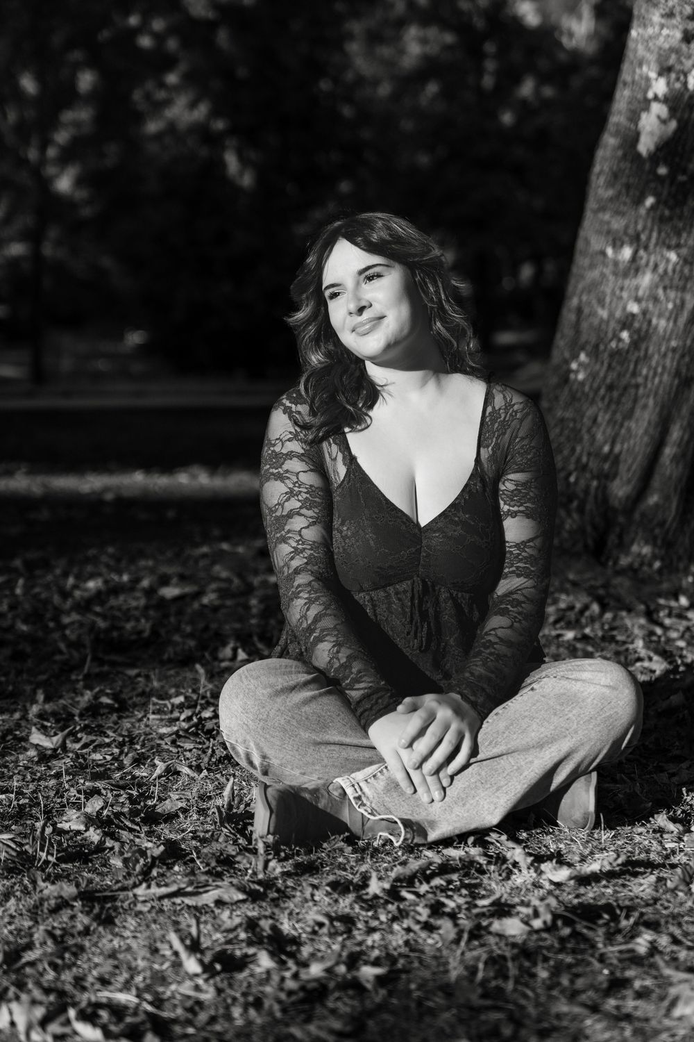 Black and white outdoor portrait sitting cross-legged under trees.